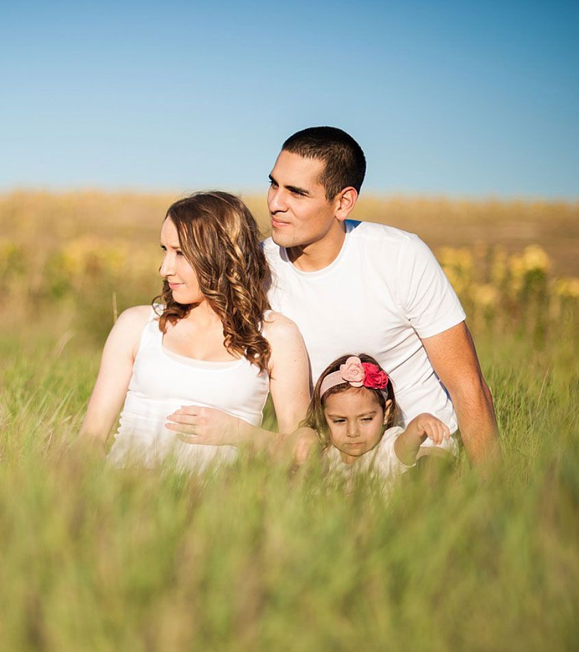 a couple and their little daughter sitting in a field