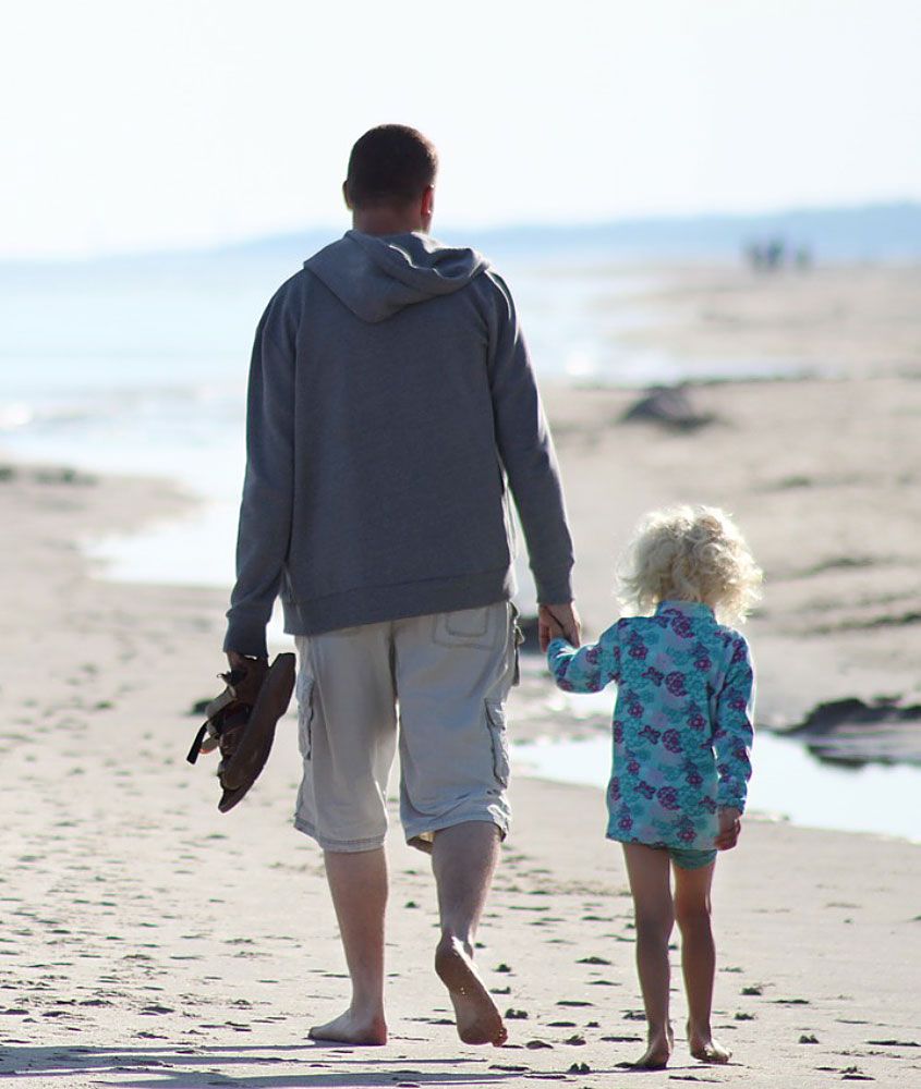 father and daughter holding hands and walking down a beach