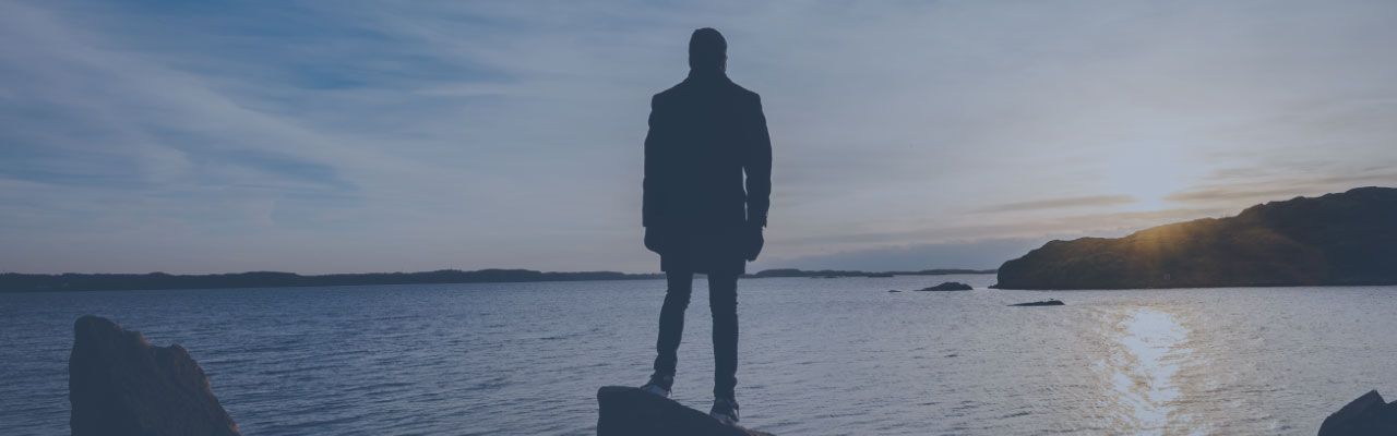 banner image of a man looking out to a lake with the sun setting